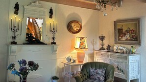 Una habitación acogedora con techo de madera, un sillón verde, una mesa blanca y una araña.