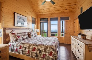 Une chambre dans une cabane en bois, avec un lit, une commode et une grande fenêtre donnant sur un paysage.