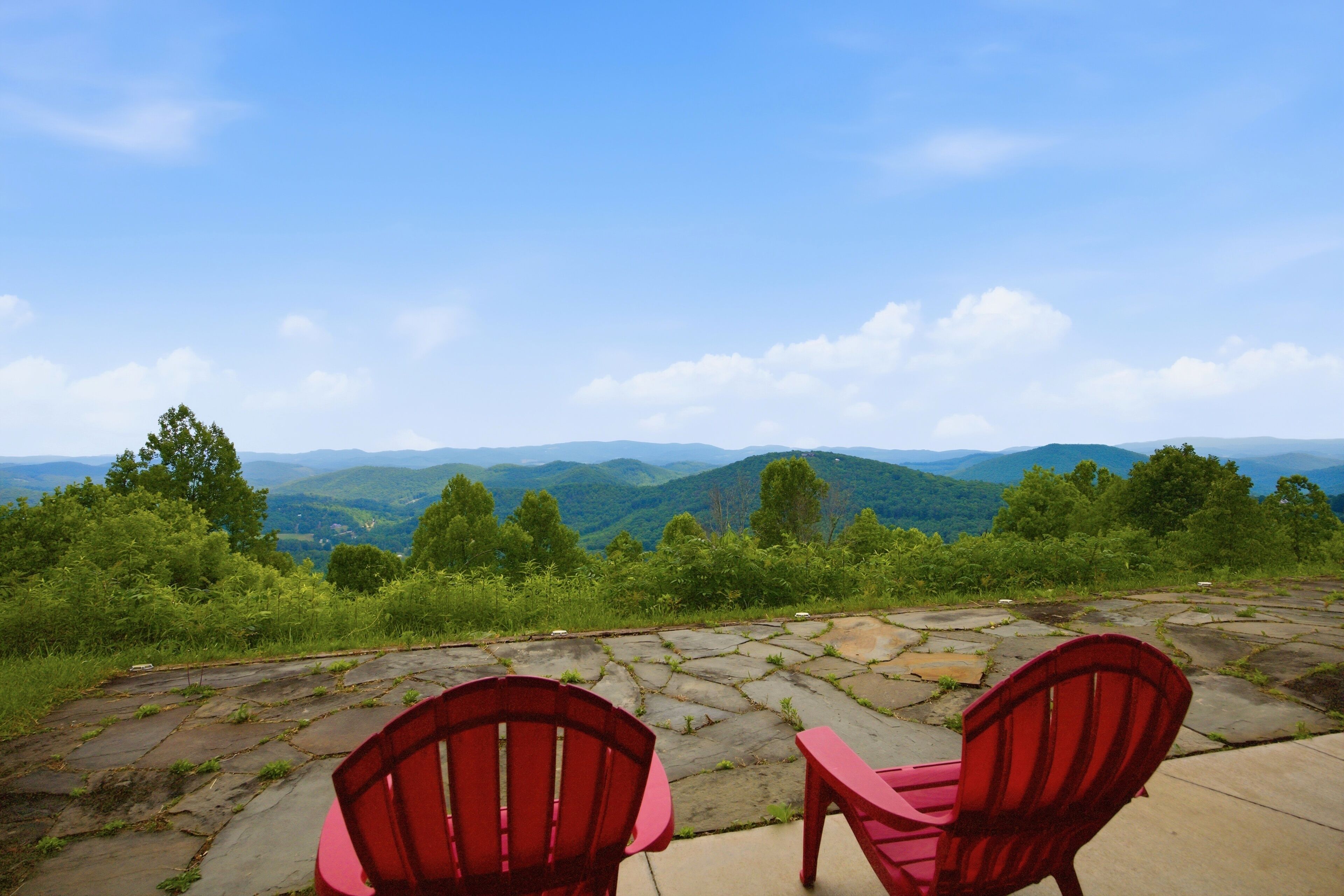 Two red chairs on a stone patio overlooking a mountainous landscape.