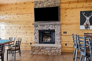 A room with a stone fireplace, wooden walls, a flat-screen TV mounted above it, and a deer painting on the wall.
