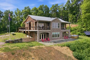 Une cabane en rondins à deux étages, dotée d’un balcon, d’une façade en pierre et d’une terrasse avec des fauteuils Adirondack.