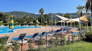 A poolside area with sun loungers and umbrellas, surrounded by palm trees and a view of a mountain range. - Large 2 bedroom apartment close to swimming pool and beaches (Contrada Difesa II)