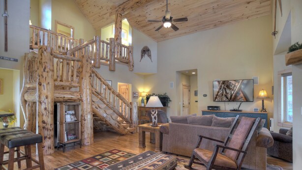 Un vaste salon agrémenté d’un escalier en bois, d’un grand téléviseur à écran plat et d’un coin salon confortable avec un tapis à motifs.