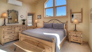 Une chambre à coucher avec un lit en bois, des tables de chevet, une commode, un miroir et une fenêtre donnant sur un paysage agréable.