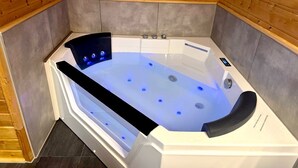 Moderni spa-huone, jossa on suuri, kirkas poreallas, puupaneloidut seinät ja laatoitettu lattia.