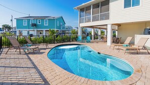 Une piscine avec des chaises longues, un patio couvert et une maison à deux étages dotée d’un balcon.