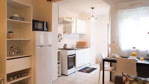 A compact kitchen with white cabinets, a microwave, an oven, and a dining area with a table and chairs. - Apartment for 2/3 people - Ney District, Angers (Angers)