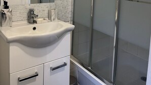 Ein Badezimmer mit Waschbecken, Spiegel und Duschkabine aus Glas.
