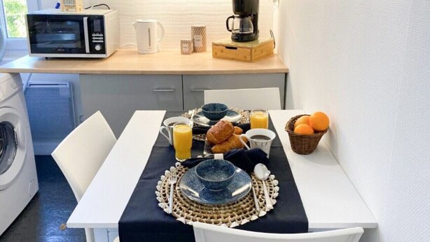 Eine kompakte Küche mit Mikrowelle, Kaffeemaschine und einem Esstisch, gedeckt mit Croissants, Orangensaft und einer Obstschale.