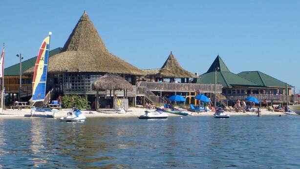 Ein Hotel am Strand mit strohgedeckten Gebäuden, einem Steg und Liegestühlen.