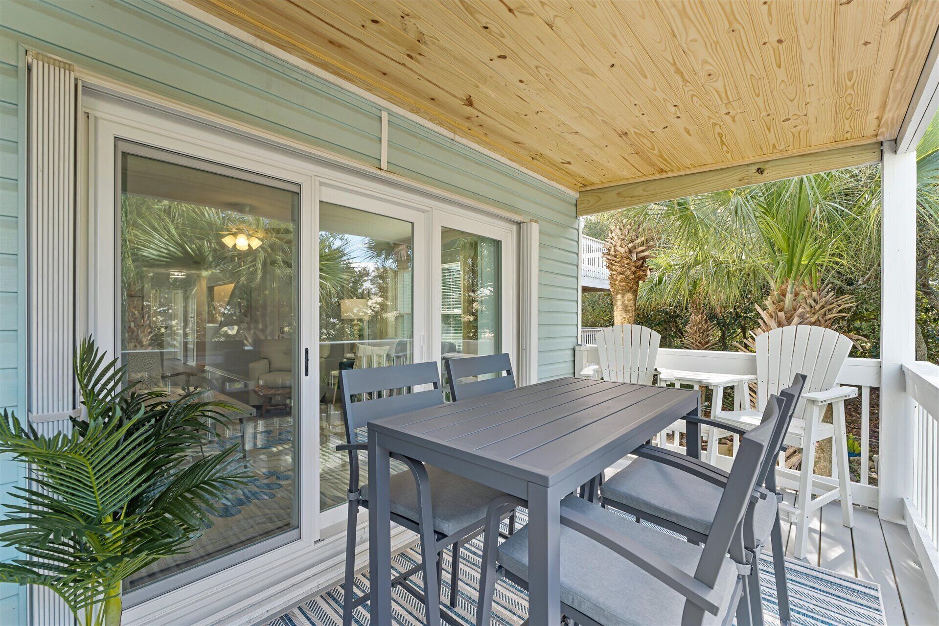 A covered patio with a table and chairs, large sliding glass doors, and a view of the surrounding greenery.