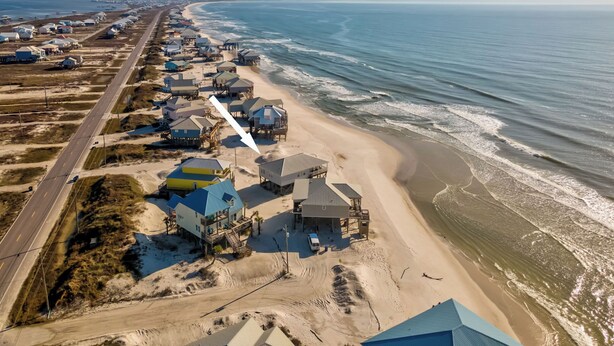 An aerial view of a coastal residential area with houses on stilts, a beach, and a road running parallel to the shore. - Simple Pleasures, Gulf Beachfront, 3 Bedroom, 2 Bath (Dauphin Island)