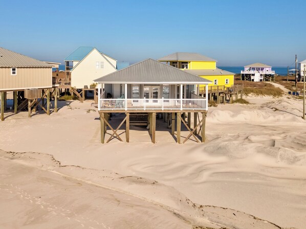 A beach house with a balcony, wooden deck, and a sandy beach in the background. - Simple Pleasures, Gulf Beachfront, 3 Bedroom, 2 Bath (Dauphin Island)