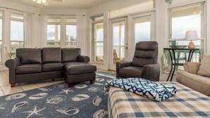 A spacious living room with a dark leather sofa, a matching armchair, and a beige sofa. A patterned rug is on the floor, and a ceiling fan is visible. - Simple Pleasures, Gulf Beachfront, 3 Bedroom, 2 Bath (Dauphin Island)
