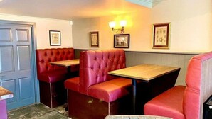 A restaurant interior with red booths and tables, framed pictures on the walls, and a blue door. - The George Inn Plympton (Plymouth)
