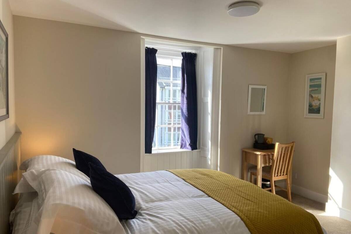Une chambre à coucher avec un lit, une fenêtre avec des rideaux, une chaise et une petite table avec une lampe.