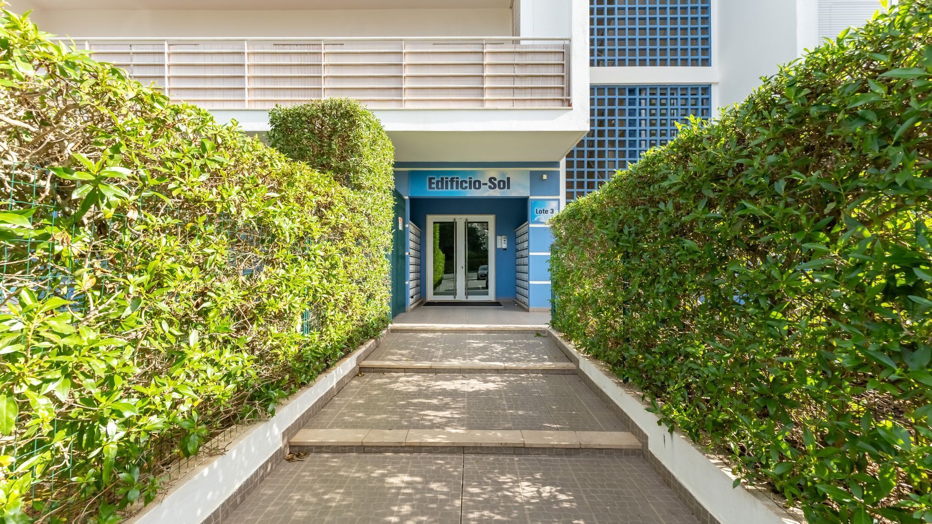 A pathway leading to a building entrance labeled "Edificio-Sol" with a modern architectural design, featuring a blue and white color scheme and a gated entrance.