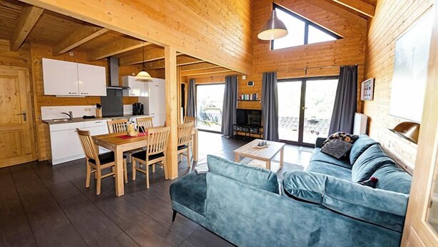 A wooden cabin interior with a dining area, sofa, and kitchen.