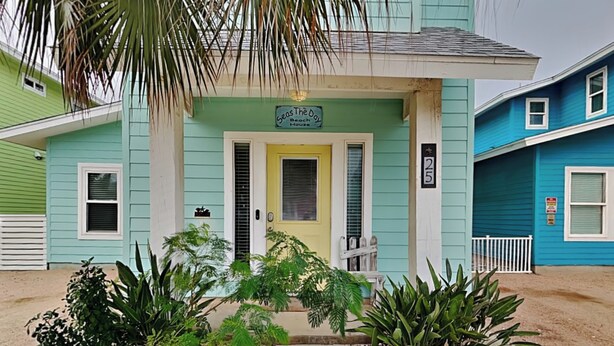 Un bâtiment à deux étages avec une porte jaune et une enseigne sur laquelle on peut lire : « Seas The Day Beach House ».