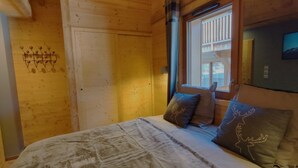Ein Holzhütten-Zimmer mit einem Bett, zwei Kissen mit Hirschmotiven, einem Fenster und einer Holzwand mit einer verzierten Metallleiste.