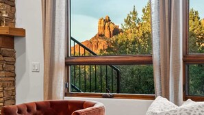 A room with a large window, a stone wall, a red chair, and a patterned sofa. - Luxury Sedona Sanctuary | Views, Sauna, Fire Pit (Sedona)