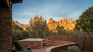 A stone patio with a hot tub, outdoor seating, and a view of a mountainous landscape. - Luxury Sedona Sanctuary | Views, Sauna, Fire Pit (Sedona)