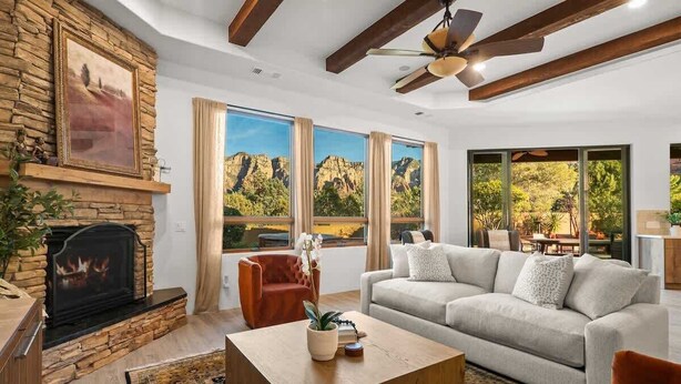 A living room with a fireplace, a sofa, a coffee table, and large windows with a mountain view. - Luxury Sedona Sanctuary | Views, Sauna, Fire Pit (Sedona)