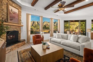 Ein Wohnzimmer mit Kamin, einer Couch, einem Couchtisch und großen Fenstern mit Blick auf die Berge.
