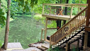 Un pontile in legno con una scala che conduce a una piattaforma panoramica su un corpo d'acqua, circondata da alberi.
