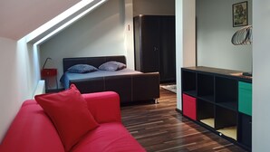 A modern loft bedroom with a sloped ceiling, a bed with dark headboard, a red sofa, and a built-in desk with shelving. - 3-room 2 level family-/pet-friendly apartment in Riga with WiFi and parking (Riga)