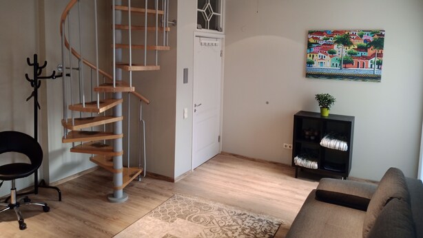 A living room with a spiral staircase, a ceiling fan, a sofa, a coffee table, and a painting on the wall. - 3-room 2 level family-/pet-friendly apartment in Riga with WiFi and parking (Riga)