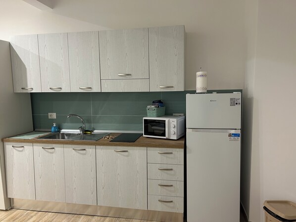 Une cuisine moderne avec des meubles de couleur bois clair, un évier en acier inoxydable, un four à micro-ondes et un réfrigérateur blanc.
