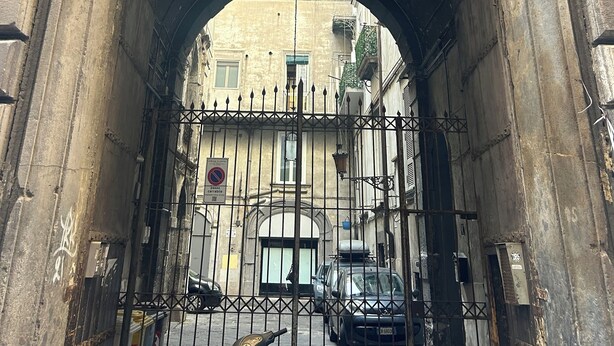 An arched stone gateway with a metal gate, leading to a building with a yellow facade and a black car parked in front. - Le Suite di Giordy e Peppe 
4-bedroom apartment in charming Napoli with WiFi, AC (Napoli)