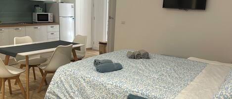 Une chambre avec un lit, une télévision, un bureau et un coin cuisine.