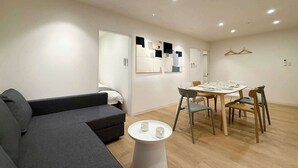 Ein modernes Wohnzimmer mit einem grauen Sofa, einem Esstisch mit Stühlen und einem kleinen weißen Beistelltisch.