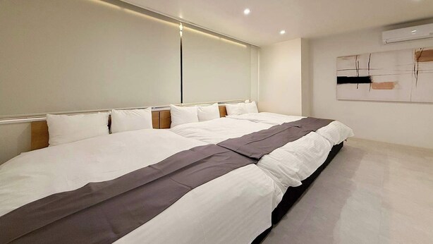 A modern hotel room with two beds, a large window, and a minimalist design.