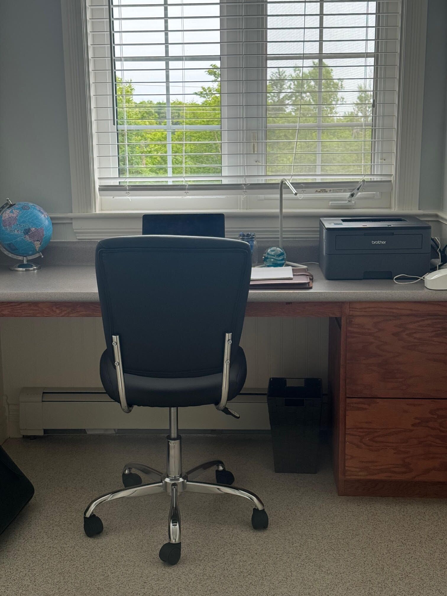 Un bureau à domicile équipé d’un bureau, d’une chaise, d’un globe terrestre, d’une imprimante et d’une fenêtre avec des stores.