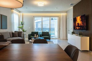 Una sala de estar moderna con una mesa de comedor, sofás, un televisor y un balcón con vistas.