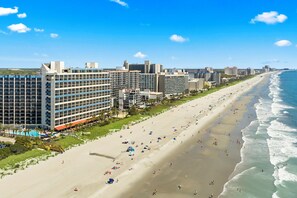 Un hôtel en bord de mer, avec plusieurs étages, une plage en premier plan et une vue sur l’océan.