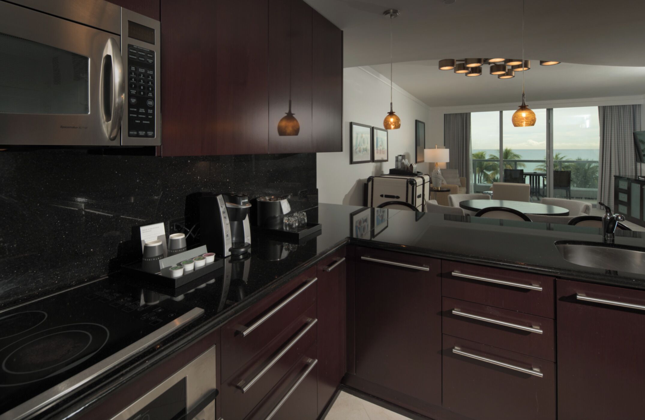 A modern kitchen with dark wood cabinets, stainless steel appliances, and a black granite countertop. There is a coffee machine and a toaster on the counter.