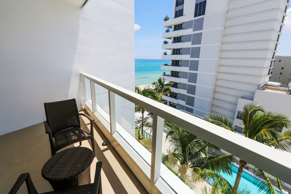 A balcony with wicker furniture overlooking a pool and a view of the ocean.