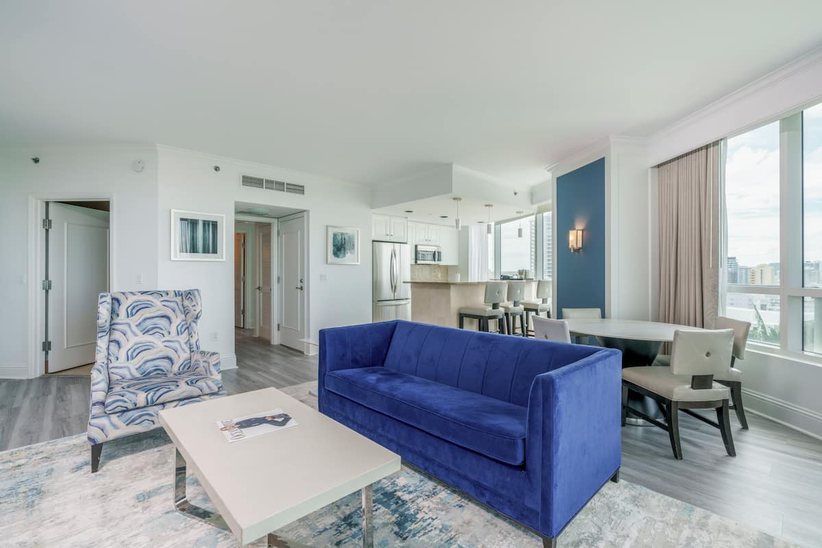 A modern living room with a blue sofa, a patterned armchair, and a dining area with a table and chairs.