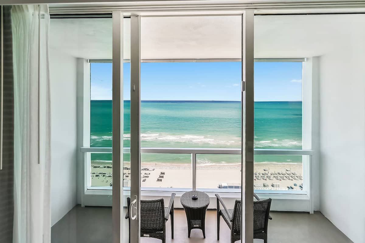 A balcony with a view of the ocean and beach, furnished with wicker chairs and a small table.