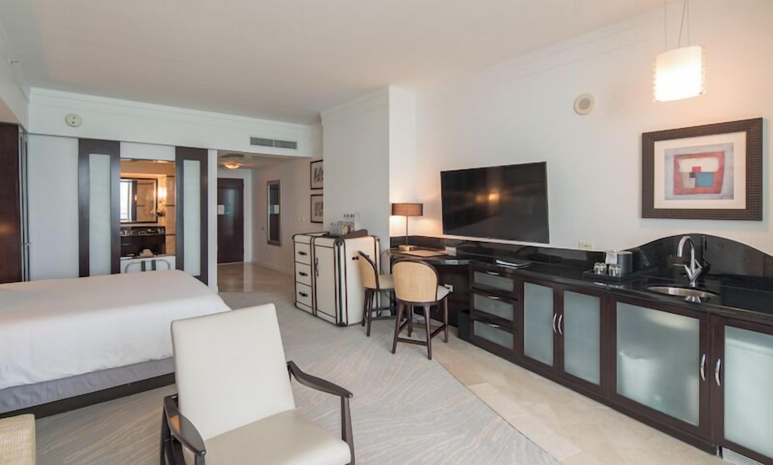 Ein Hotelzimmer mit einem großen Bett, einem Schreibtisch mit Stuhl, einem Fernseher und einer Küchenzeile.