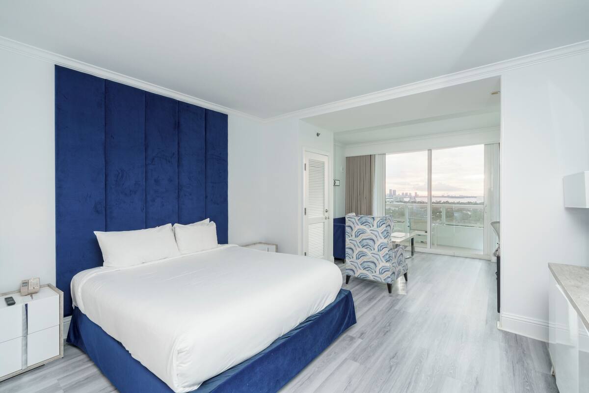 A modern hotel room with a large bed, a view of the city, and a balcony.