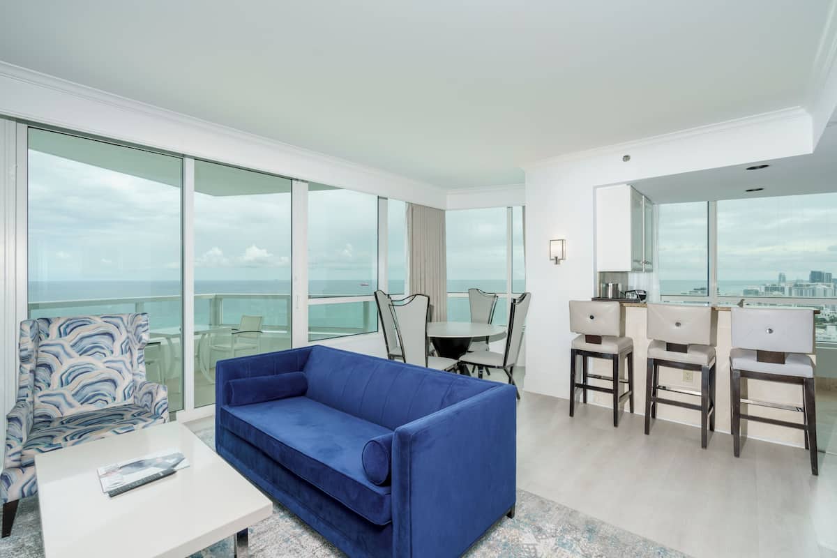A modern living room with a blue sofa, a white coffee table, and a dining area with a table and chairs.