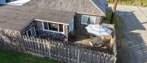 Een huis met twee verdiepingen, een schuin dak, een omheinde achtertuin en een terras met tuinmeubels.