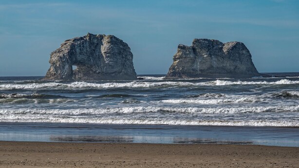 Une plage bordée de deux formations rocheuses imposantes qui émergent de l’océan.