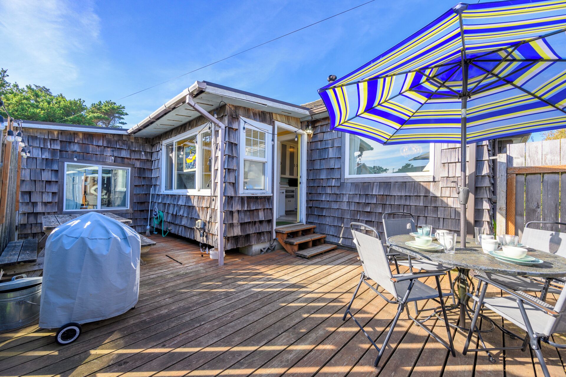 A wooden deck with a grill, a table with chairs, and a striped umbrella.