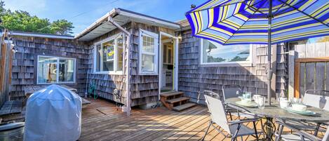 A wooden deck with a grill, a table with chairs, and a striped umbrella.